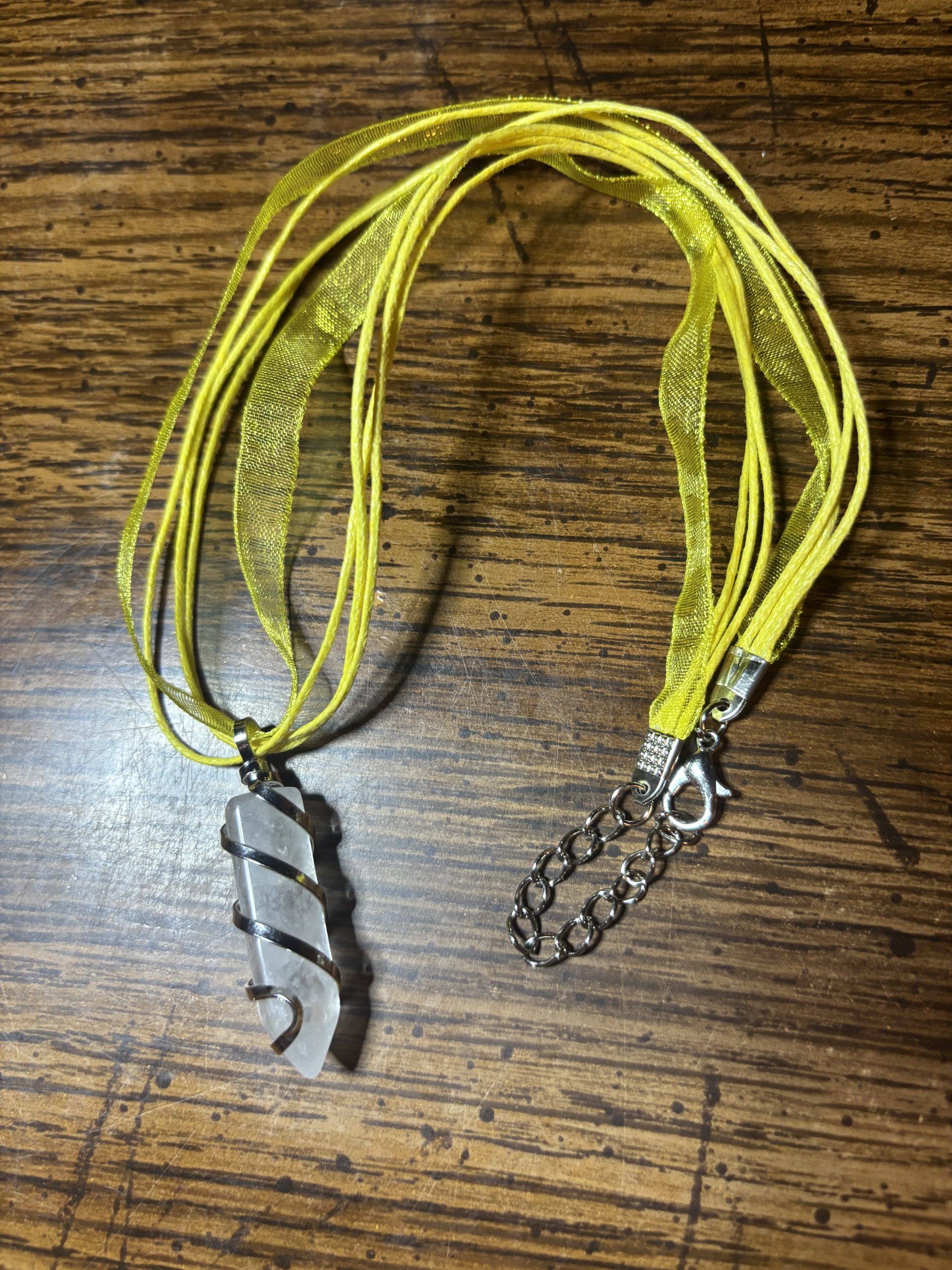 Yellow ribbon necklace with a translucent spiral pendant wrapped in metal, on a wooden surface