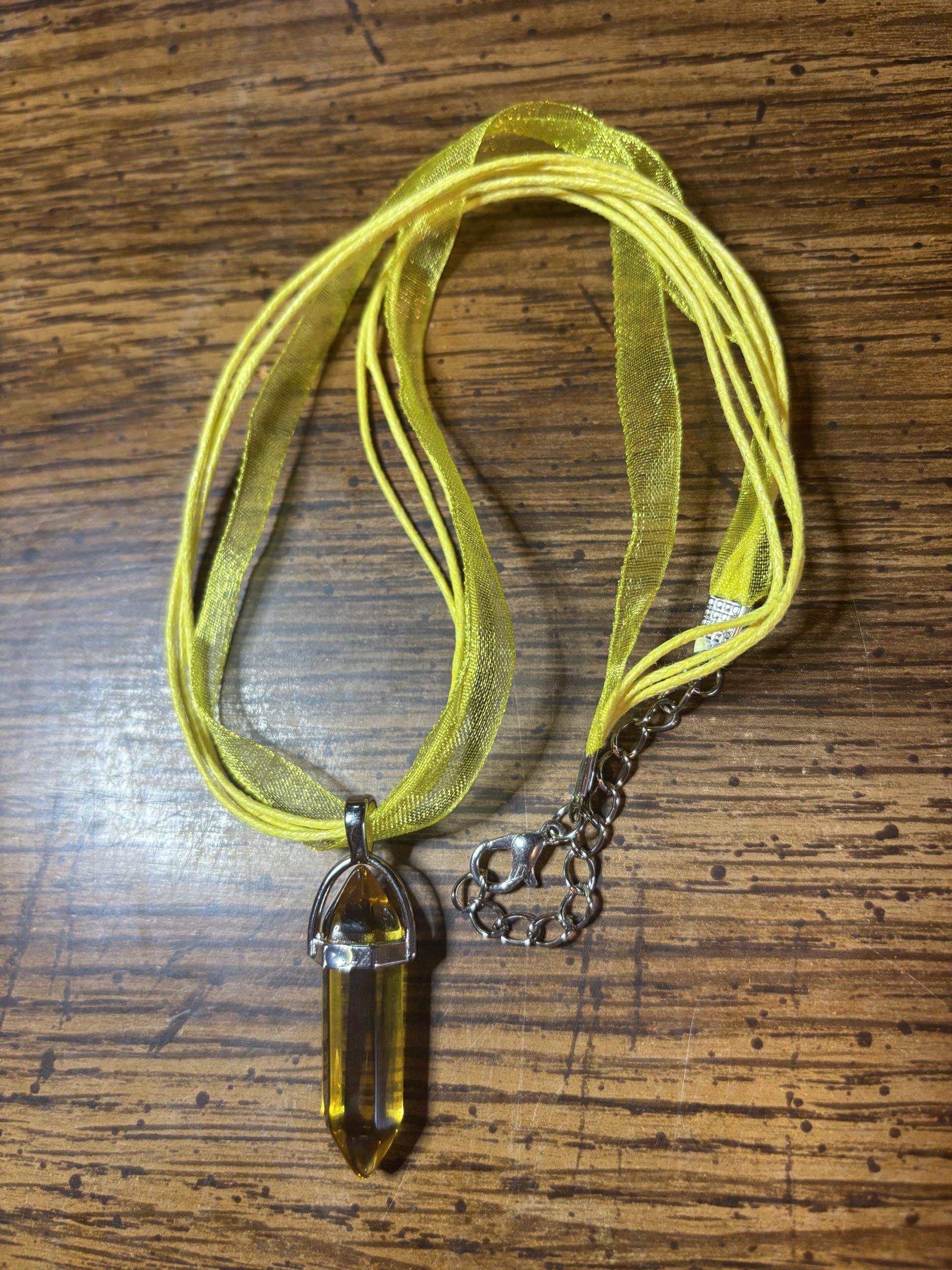 Lime ribbon necklace with a yellow crystal pendant on a wooden surface.